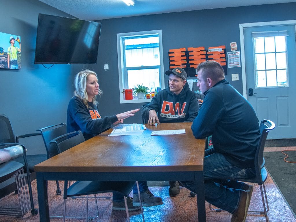 Three people sitting at a table in front of a tv.