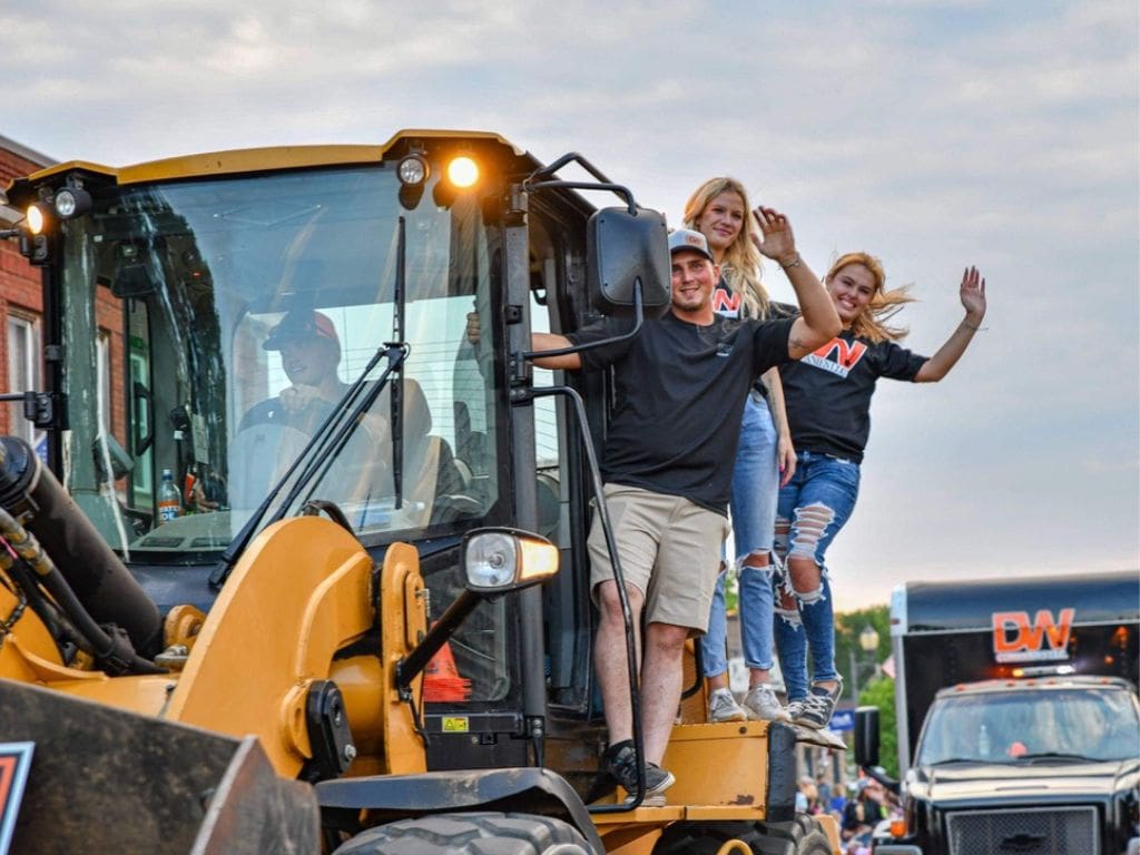 A group of people riding on the back of a yellow tractor.