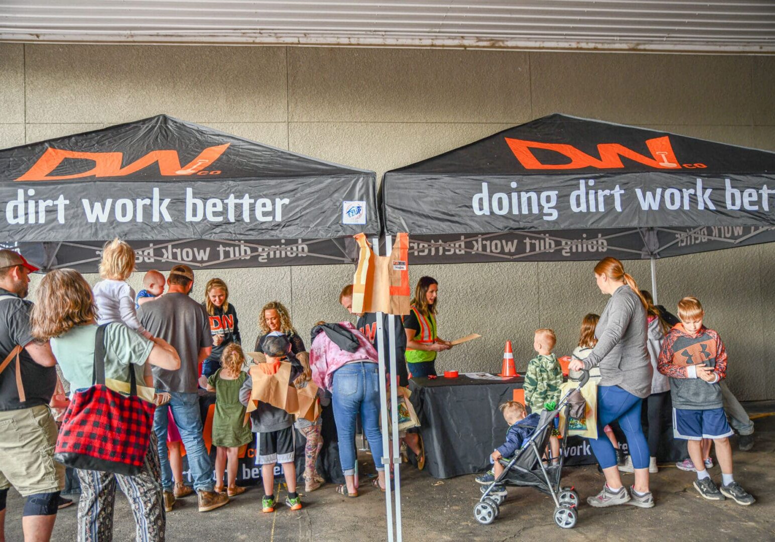 A group of people standing under two black and orange tents.